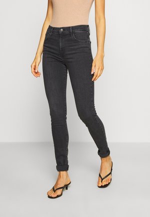 Un jean skinny noir présente une taille haute, un design à cinq poches et des poignets retroussés, fabriqué à partir de denim au toucher lisse. Associé avec des tongs noires.