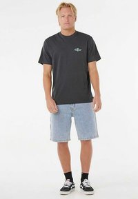 Camiseta negra de algodón con mangas cortas, con un pequeño logo turquesa en el pecho, combinada con shorts de mezclilla azul claro y zapatillas negras.