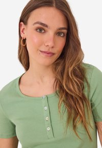 T-shirt à rayures vert clair avec un col rond, comportant une rangée de cinq boutons à l'avant et des manches courtes. Texture lisse.