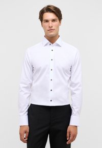 Witte button-down blouse met een klassieke kraag en bruine knopen, voorzien van lange mouwen en een gladde, gestructureerde stof.