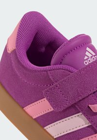Sneaker in suede viola con dettagli rosa e suola in gomma. Caratterizzato da una fascia in Velcro, rivestimento in mesh testurizzato e tre strisce bianche sul lato.