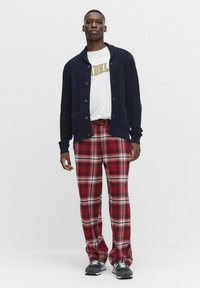 Marineblauwe cardigan met knopen, wit t-shirt met gele letters en rood geruite broek. Sneakers maken de outfit compleet.