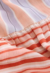 Tissu avec couture froncée présentant des rayures horizontales dans des tons pêche, lavande, blanc et rouge.