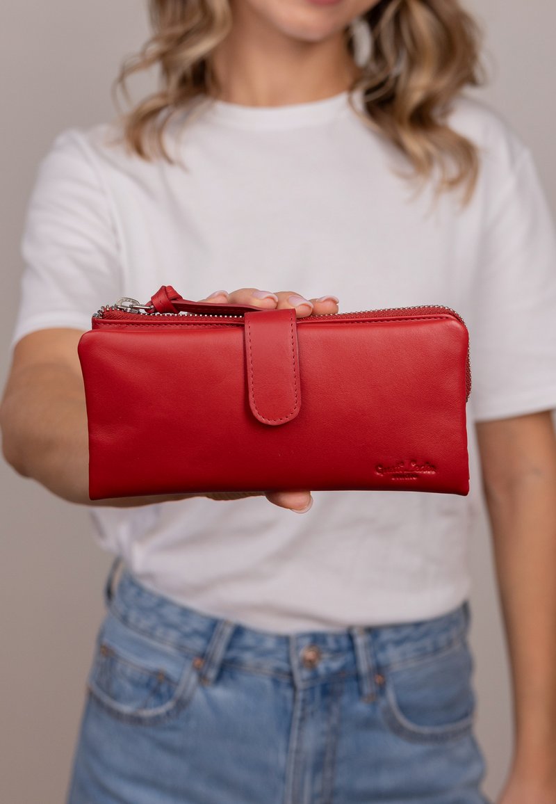 Cartera de piel roja con textura suave, cierre de cremallera y una lengüeta de botón a juego. Logo grabado en el lateral.