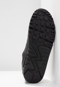 Czarną podeszwę Nike z teksturowanej gumy, z falistym wzorem i wyraźnym bieżnikiem, z wyraźnie widocznym logo Nike.