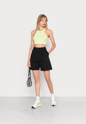 Top cropped canelado verde claro combinado com calções pretos de cintura alta. Acessórios incluem uma bolsa listrada e sapatilhas brancas desportivas.
