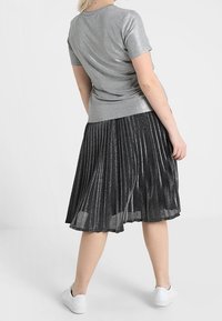 Silver short-sleeve top with a fitted silhouette paired with a pleated black skirt featuring a metallic finish and knee-length hem. White shoes.