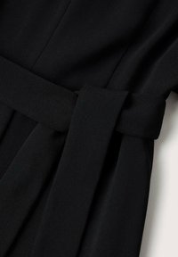 Vêtement en tissu noir avec une large ceinture nouée à la taille. Le matériau a une texture lisse avec un design soigné et des lignes épurées.