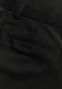 Czarne spodnie wykonane z tkaniny plecionej, z tylną kieszenią o pionowym otwarciu i drobnymi detalami przeszyć, gładką teksturą oraz dopasowanym pasem.