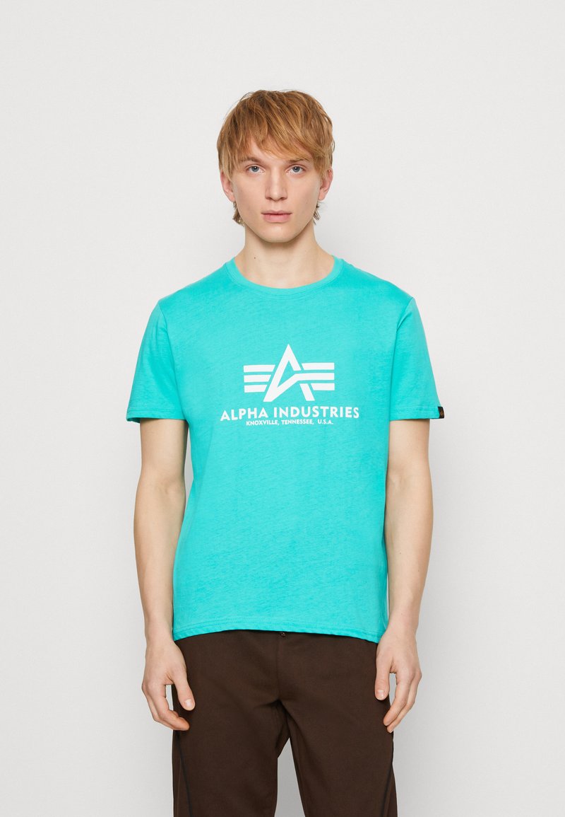 Camiseta de cuello redondo color turquesa, hecha de algodón, con un estampado de logo blanco y mangas cortas. La tela tiene un acabado suave y ligeramente texturizado.