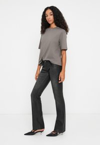 Grå t-skjorte med korte ermer og perledetalj ved halsen, kombinert med svarte utsvingte jeans og svarte spissede hæler. Glatt stoff med en svak glans.
