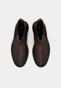 Pantofi slip-on din piele maro, cu textură netedă, vârf rotund, panouri laterale elastice și talpă din cauciuc, având un logo subtil al brandului în interior.