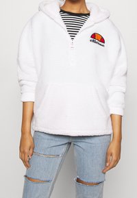 White hooded pullover sweatshirt in plush fabric, featuring a half-zip, front pouch pocket, and embroidered logo with orange and red accents.