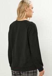 Felpa nera con scollo rotondo, maniche lunghe e vestibilità comoda. Tessuto morbido con una consistenza liscia, abbinata a pantaloni a quadri.