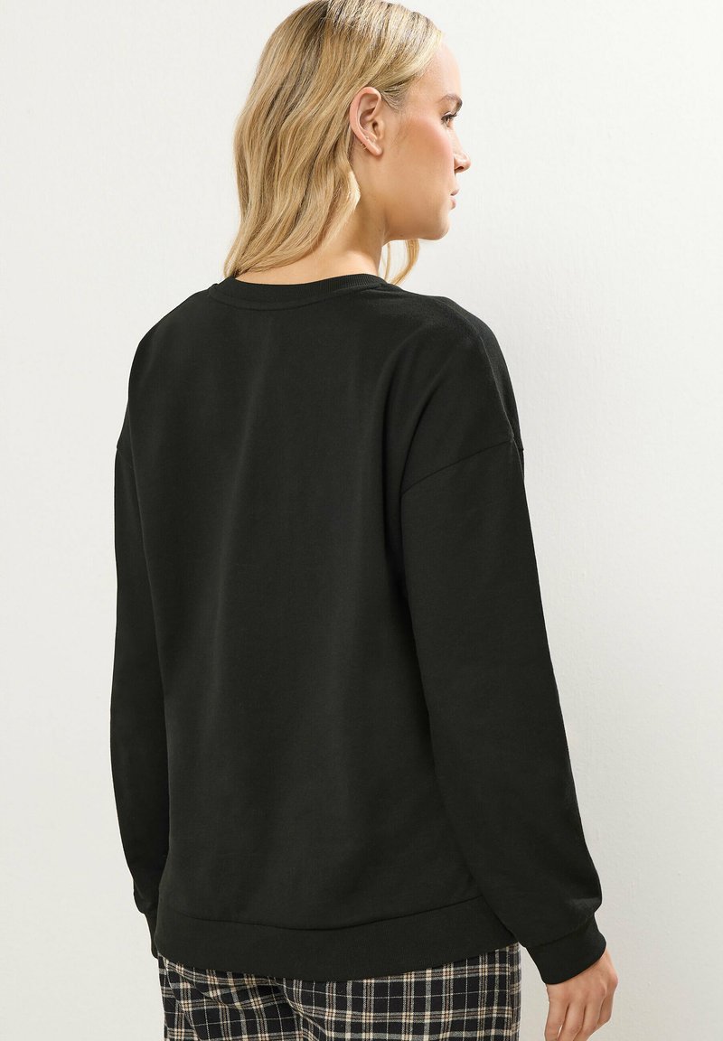 Felpa nera con scollo rotondo, maniche lunghe e vestibilità comoda. Tessuto morbido con una consistenza liscia, abbinata a pantaloni a quadri.