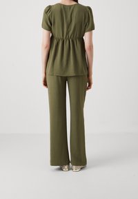 Oliwkowy, dwuczęściowy zestaw składający się z topu z krótkim rękawem i marszczoną talią oraz szerokich spodni, wykonany z lekkiego, teksturowanego materiału.
