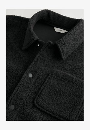 Svart texturerad fleecejacka med krage, tryckknappar och en fyrkantig bröstficka, som visar tygdetalj och varumärkesetikett på insidan.