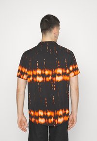 Camicetta a maniche corte in tessuto nero con un motivo astratto arancione e bianco, colletto button-down e orlo curvo.