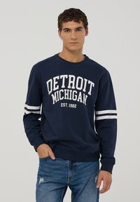 Granatowy sweatshirt z napisem "DETROIT MICHIGAN" oraz "EST. 1982" w kolorze białym, z białymi paskami na rękawach.