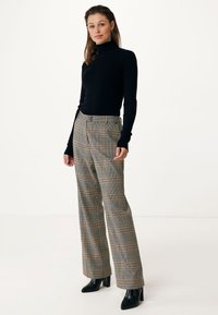 Black turtleneck sweater paired with high-waisted plaid trousers featuring brown and cream accents, and black block-heeled ankle boots.