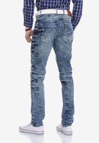 Lichtblauwe denim jeans met een slim fit, voorzien van schuin geplaatste achterzakken en een iets vervaagde afwerking, vergezeld van een witte riem.