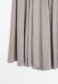Gray pleated fabric skirt with vertical stripes and a textured surface. Features a flowing design and a hem that curves gently.