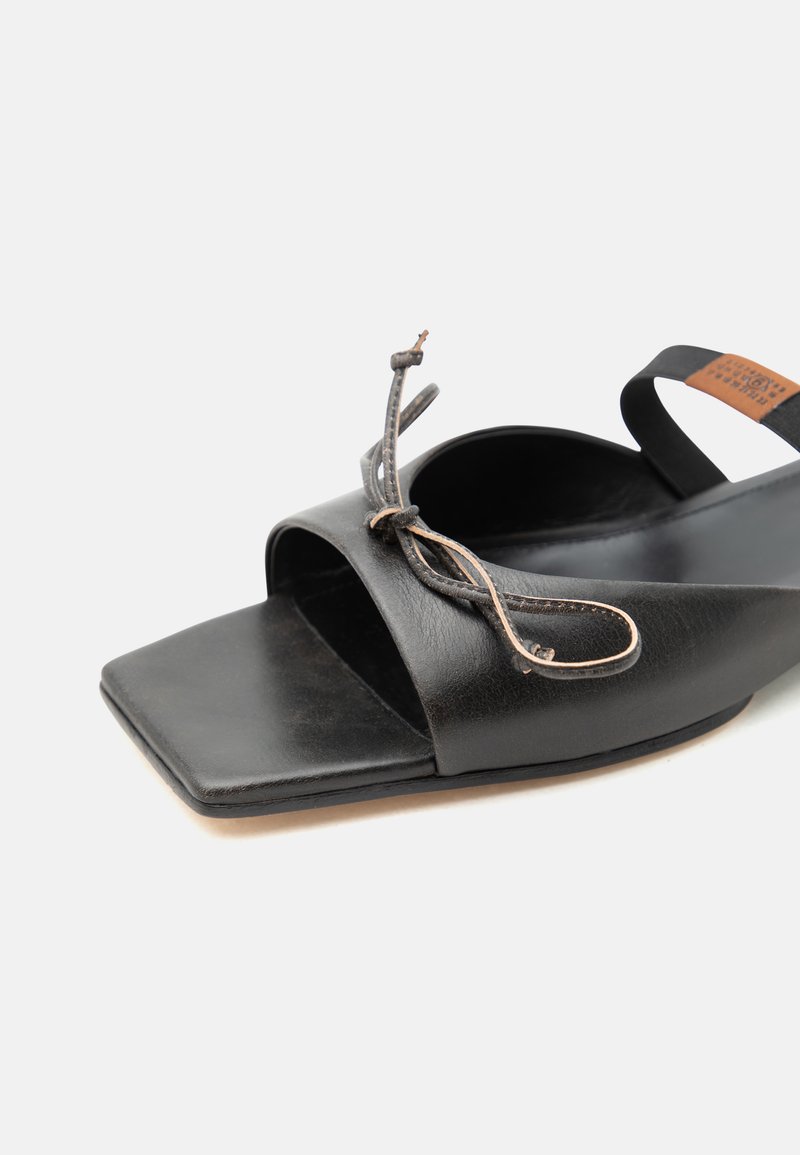 Sandalia abierta de cuero negro con punta cuadrada, detalle de un lazo anudado en la correa y una correa trasera con una pequeña etiqueta.
