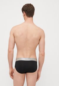 Schwarze Unterwäsche mit einem silbernen Calvin Klein Bund, die eine glatte Textur und ein schlichtes Design aufweist, von hinten gezeigt.