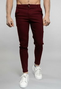Pantalons slim-fit bourgogne avec une taille plate, une fermeture à un bouton et des poches latérales, associés à des baskets blanches.