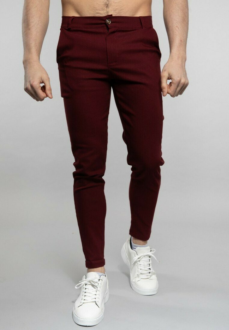 Pantalons slim-fit bourgogne avec une taille plate, une fermeture à un bouton et des poches latérales, associés à des baskets blanches.