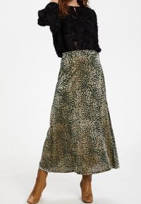 Maxi sukně v zeleném a béžovém leopardím vzoru, vyrobená z lehké látky. Má vzdušný střih, doplněná černým texturovaným topem a hnědými kotníkovými botami.