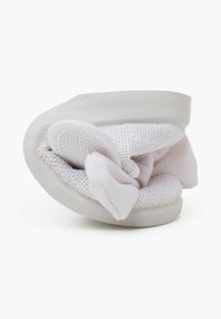 Zapato de tela blanco estilo slip-on con una banda elástica gruesa, textura de malla suave y una suela redondeada y flexible. El diseño es compacto y plegable.