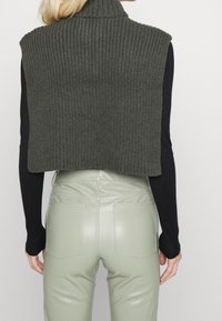 Maglione senza maniche in verde scuro con colletto alto, abbinato a pantaloni in pelle verde chiaro a vita alta e attillati.