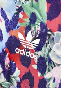 Bavlněná látka s květinovým vzorem v živých barvách, s výraznými zelenými, červenými a modrými odstíny. Obsahuje bílé logo Adidas se třemi pruhy.