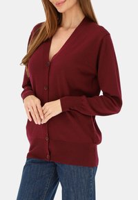 Bordowy kardigan z dekoltem w serek, z przodu na guziki i z długimi rękawami. Miękka dzianina z prążkowanymi mankietami i dołem. Luźne, casualowe dopasowanie.