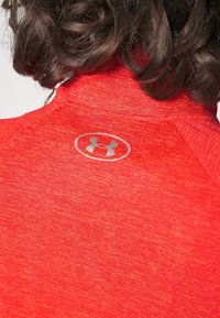 Rood, gestructureerd sportshirt met een hoge kraag en korte mouwen. Heeft een zilveren logo op de rug. Het materiaal lijkt lichtgewicht en ademend.