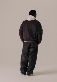 Black bomber jacket with a white hooded lining, paired with loose black leather pants and white sneakers, viewed from the back.