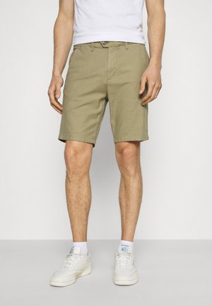 Shorts kaki en tissu léger avec une coupe droite, des poches avant et une fermeture à bouton. Portés avec des baskets blanches et des chaussettes.