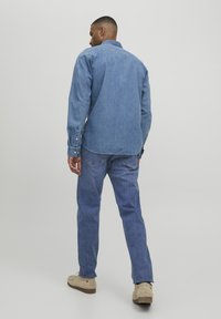 Camisa de mezclilla azul clara con mangas largas y puños abotonados; combinada con jeans de mezclilla azul a juego y calzado beige. Diseño sencillo, ajuste casual.