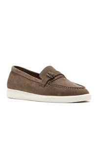 Scarpe slip-on in suede marrone con suola in gomma, cuciture in stile mocassino e un accento decorativo in pelle sulla tomaia.