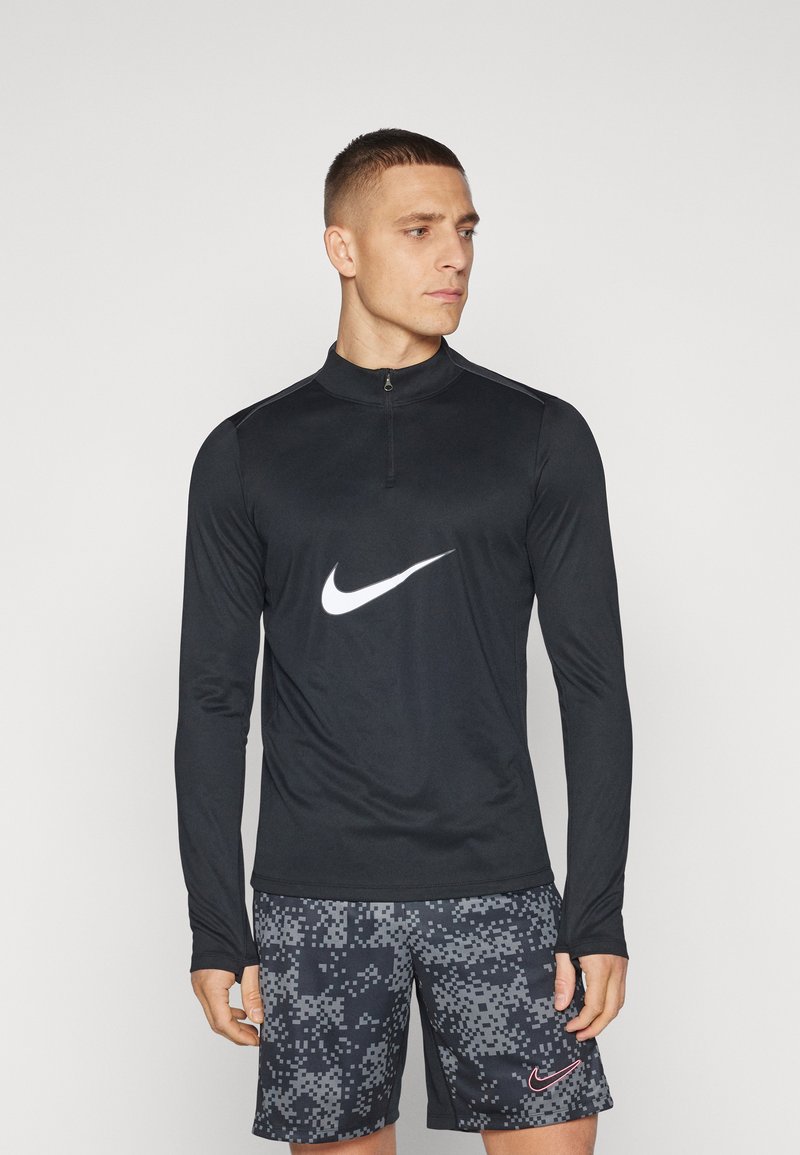 Uomo in cima a maniche lunghe nera con zip con il logo Nike bianco e pantaloni corti neri con motivo camo digitale e logo Nike rosa.