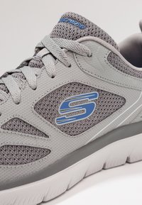 Gray athletic shoe with mesh and synthetic upper, features blue accents, rounded toe, and textured sole with prominent tread.