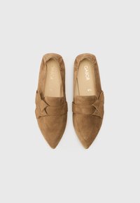 Καφέ καστόρινα παπούτσια χωρίς κορδόνια με μυτερή μύτη και διακοσμητικό κόμπο στο μπροστινό μέρος. Μαλακή επένδυση και διακριτικές ραφές ως διακοσμητικά στοιχεία.