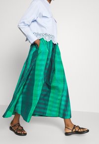 Vilkkuma green plaid maxi skirt with pockets, coupled with a light blue cropped shirt that has lace trim at the hem. Black strappy sandals.