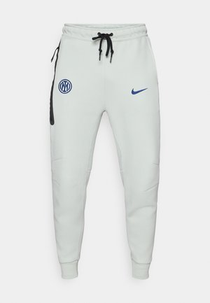 Light gray joggers made of soft fabric, featuring a black accent pocket, blue logo patches, adjustable drawstring waistband, and fitted cuffs.