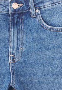 Jeans de mezclilla azul claro con una textura desgastada, pespuntes dorados y cierre frontal con botón; cuenta con un bolsillo lateral y presillas para el cinturón.