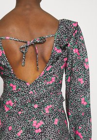 Espalda de una mujer que lleva un vestido negro con flores rosas y blancas, que presenta una espalda en V profunda y una tira atada en la parte superior de la espalda.