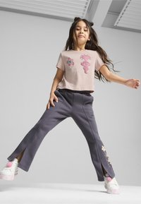 Lys rosa cropped t-shirt med blomstermotiv og karakterprint, parret med mørkegrå Bukser med sideslids og blomstermotiver ved kanten.