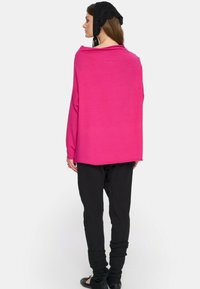 Przesadnie duży różowy sweter z długimi rękawami, szerokim dekoltem i miękką teksturą. W połączeniu z czarnymi spodniami z marszczonymi mankietami.