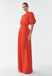 Punane, pikk ülikond puffvarrukatega, vöödiga taljes ja laia jala disainiga. Sujuv kangas voolava siluetiga. Ilma mustrite ja metallosadeta.